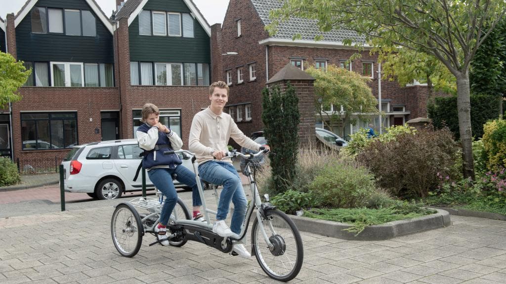 -	Een jongen zit voorop op een speciale fiets met drie wielen, achterop zit een jonge vrouw.