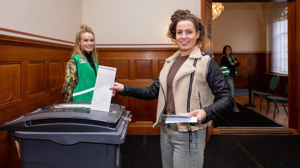 Twee vrijwilligers en een stemmer bij de stembus in een stembureau.