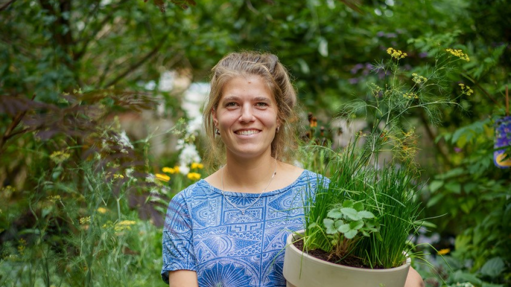 Een vrouw staat met een plantenpot in het bieslookbos.